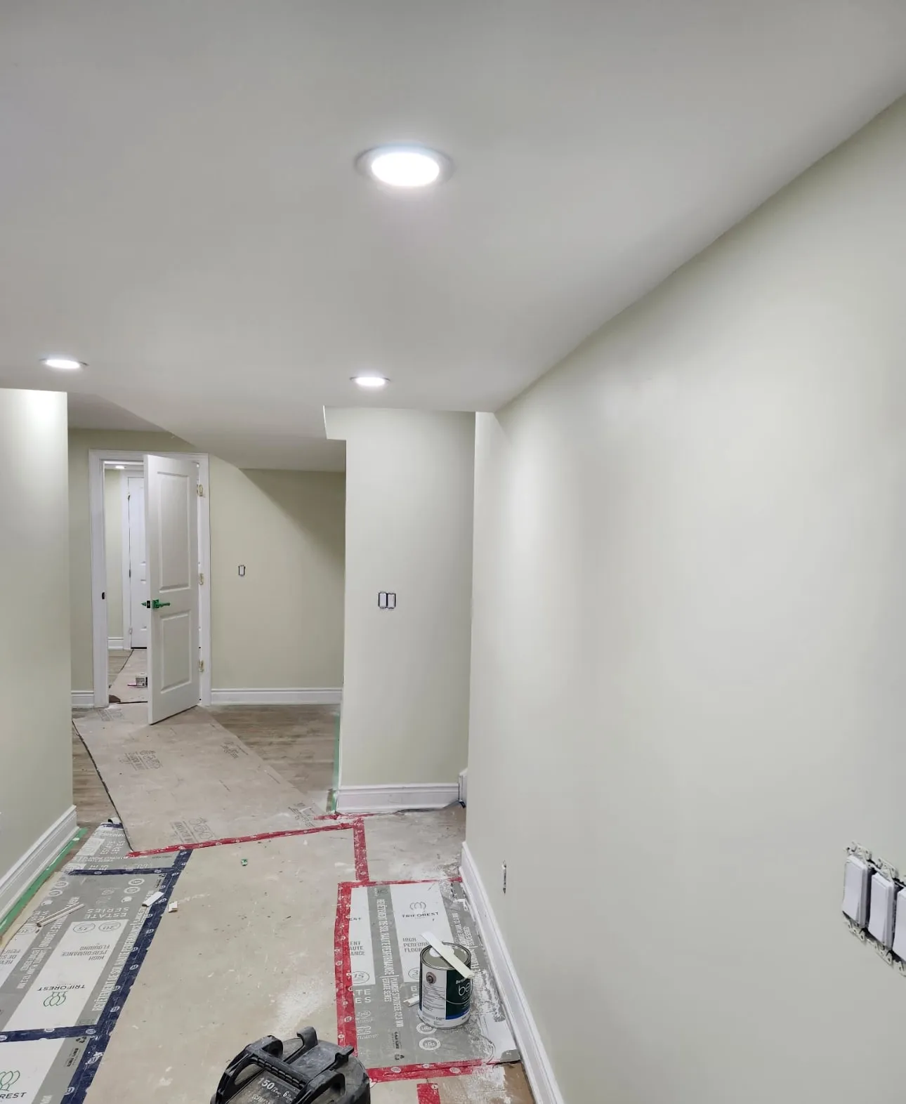 Basement hallway painted soft sage with crisp white baseboards and floors protected