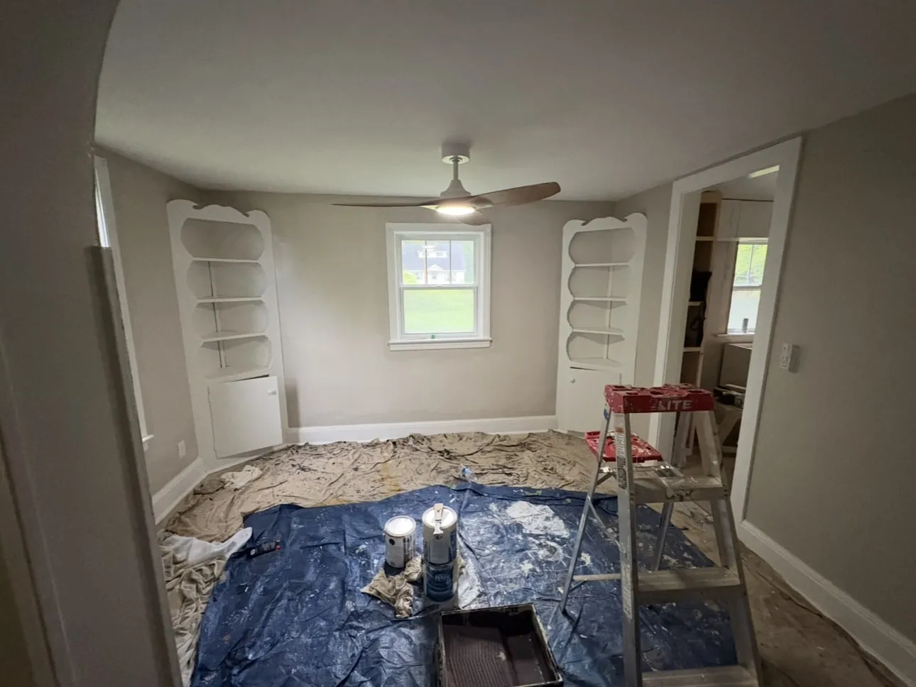 Room with white built-in shelves, floor fully covered with drop cloths before painting